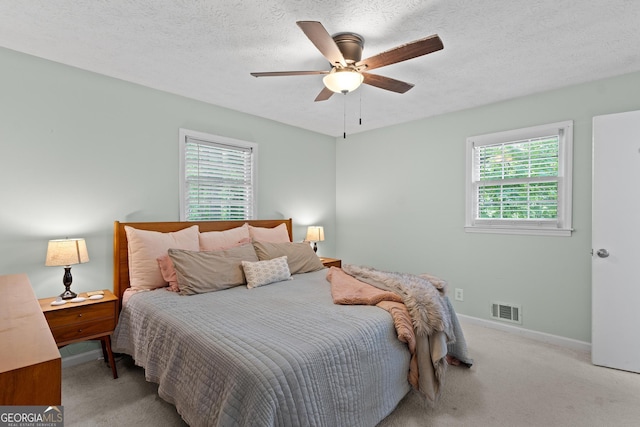 carpeted bedroom featuring a textured ceiling, visible vents, baseboards, and a ceiling fan