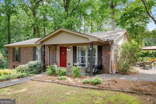 ranch-style house with a shingled roof, brick siding, and covered porch