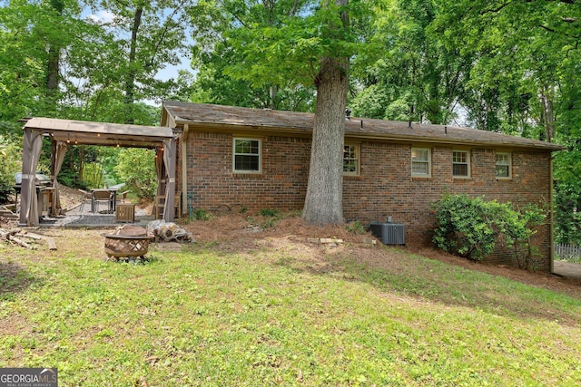 back of house featuring an outdoor fire pit, brick siding, a lawn, and central air condition unit