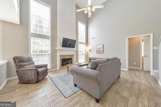living area with baseboards, light wood finished floors, a towering ceiling, and ceiling fan