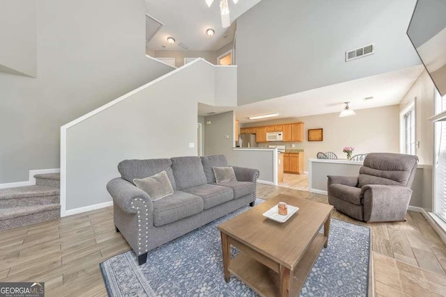 living area featuring visible vents, baseboards, a high ceiling, and stairway