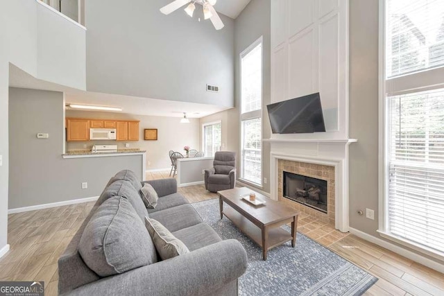 living area featuring ceiling fan, visible vents, light wood-type flooring, baseboards, and a high ceiling