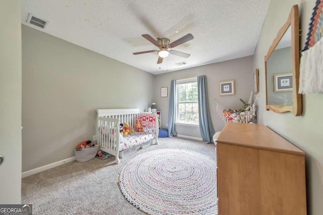 carpeted bedroom with a textured ceiling, visible vents, a crib, and baseboards