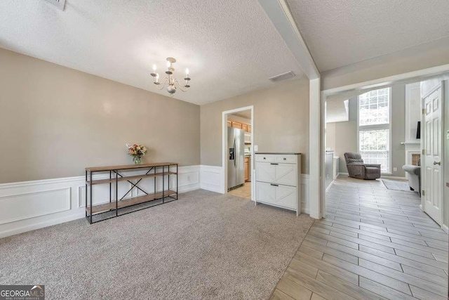 interior space with visible vents, a textured ceiling, a wainscoted wall, and a chandelier
