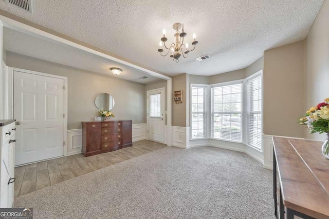 foyer with an inviting chandelier, a wainscoted wall, a textured ceiling, and visible vents