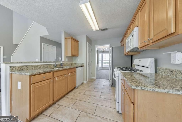 kitchen with a textured ceiling, a sink, light stone counters, a peninsula, and white appliances