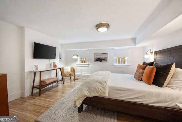 bedroom with baseboards, light wood finished floors, and a textured ceiling