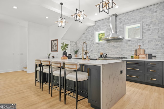 34 Candler Rd NE, Atlanta, GA 30317 - kitchen featuring a kitchen island with sink, tasteful backsplash, light stone countertops, light wood finished floors, and wall chimney exhaust hood