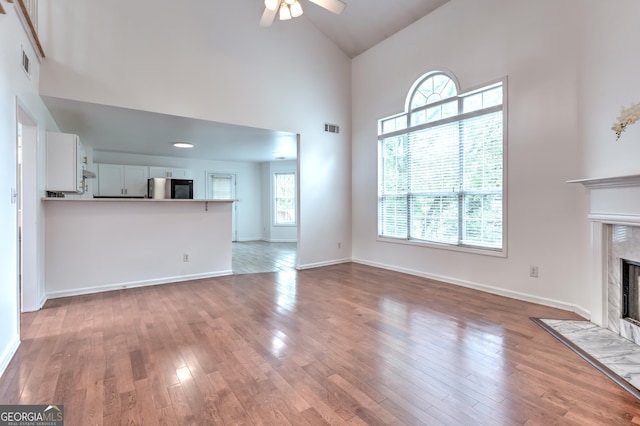 unfurnished living room with ceiling fan, visible vents, a high end fireplace, wood finished floors, and high vaulted ceiling