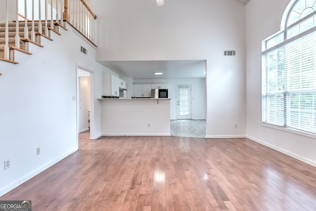 unfurnished living room featuring visible vents, light wood-style flooring, a towering ceiling, and baseboards