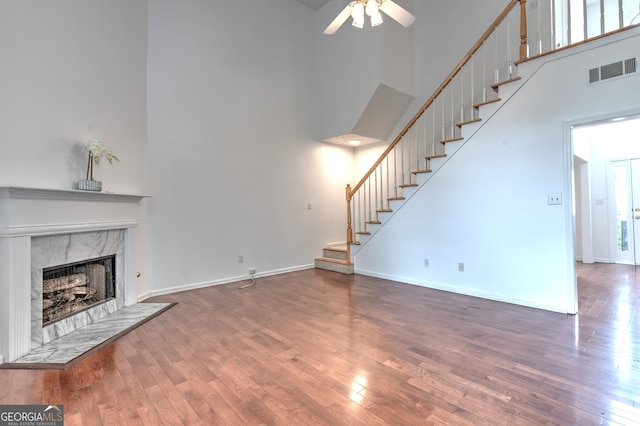 unfurnished living room featuring visible vents, wood-type flooring, a towering ceiling, a fireplace, and ceiling fan