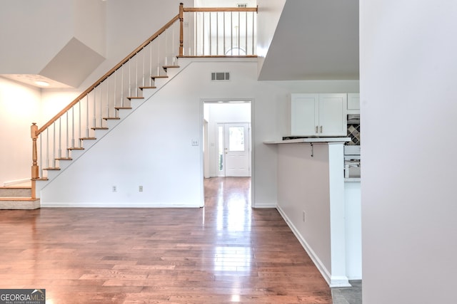 unfurnished living room featuring a towering ceiling, visible vents, wood finished floors, stairway, and baseboards