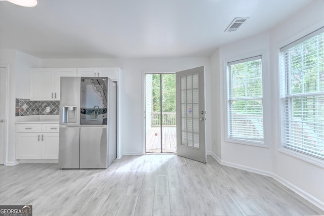 interior space with visible vents, baseboards, stainless steel fridge, light wood-type flooring, and white cabinetry