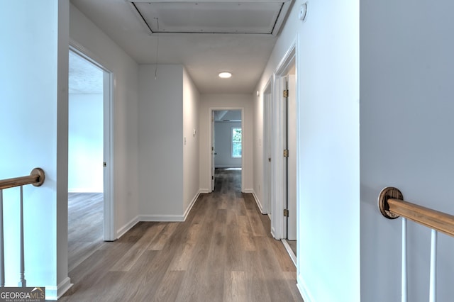 corridor with baseboards, attic access, and light wood finished floors