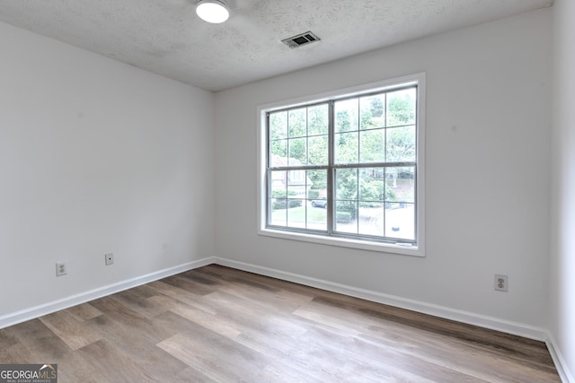 unfurnished room with a textured ceiling, baseboards, visible vents, and wood finished floors