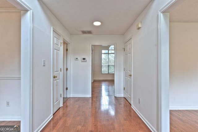 hall with visible vents, baseboards, and wood finished floors