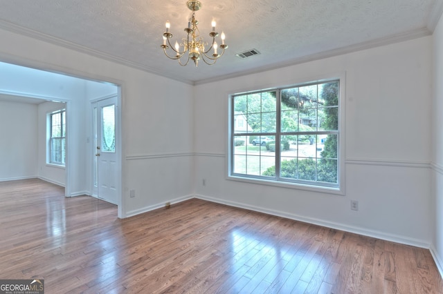 unfurnished room featuring visible vents, ornamental molding, wood finished floors, and a notable chandelier