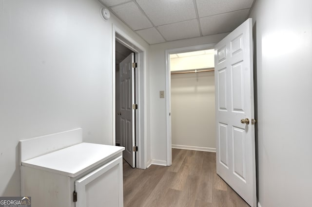 corridor featuring baseboards, a paneled ceiling, and light wood finished floors
