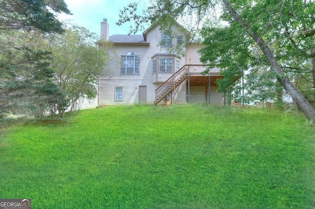 back of property with a chimney, a wooden deck, a yard, and stairway