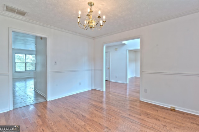 spare room with a chandelier, a textured ceiling, visible vents, and light wood-style flooring