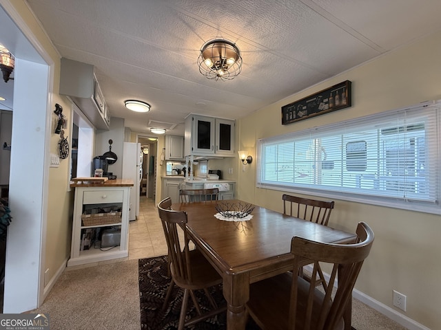 dining area featuring a textured ceiling, baseboards, light carpet, and light tile patterned floors