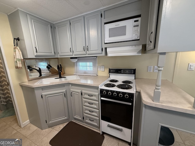 kitchen with a sink, light countertops, gray cabinets, and white appliances