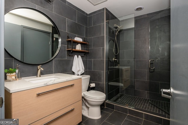 full bathroom featuring tile walls, tile patterned flooring, a shower stall, vanity, and toilet