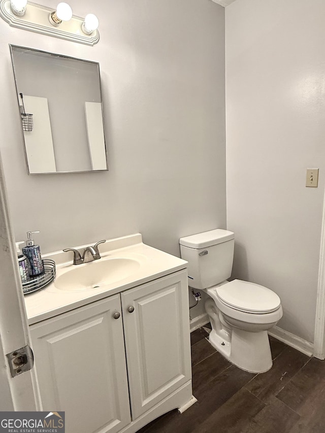 half bath featuring toilet, baseboards, wood finished floors, and vanity