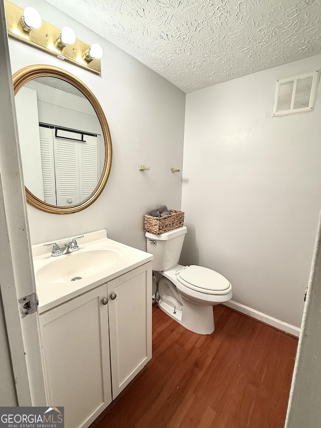 bathroom with vanity, toilet, a textured ceiling, wood finished floors, and visible vents