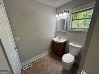 half bathroom featuring vanity, toilet, a textured ceiling, baseboards, and visible vents