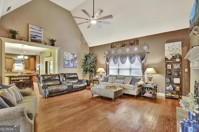 living area featuring a healthy amount of sunlight, visible vents, wood finished floors, high vaulted ceiling, and ceiling fan with notable chandelier