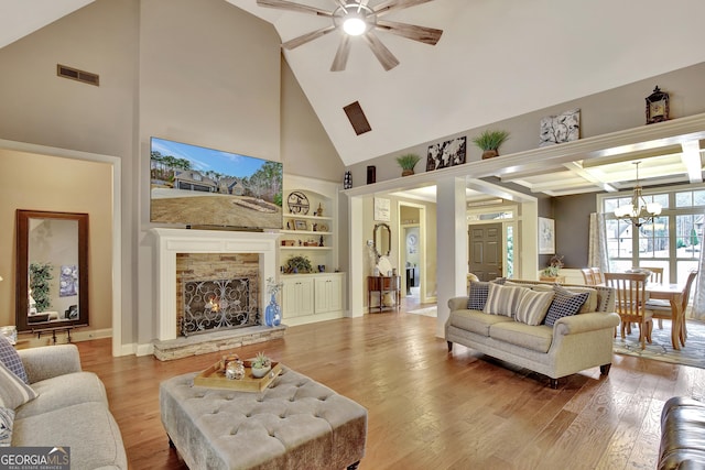 living area with high vaulted ceiling, a stone fireplace, ceiling fan with notable chandelier, and wood finished floors