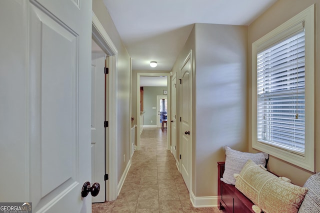 corridor with baseboards, plenty of natural light, and light tile patterned flooring