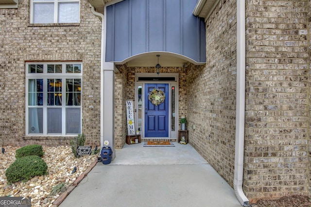 view of exterior entry featuring board and batten siding and brick siding