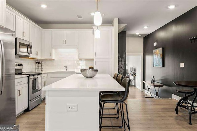 kitchen with white cabinets, appliances with stainless steel finishes, a sink, light wood-type flooring, and a kitchen bar