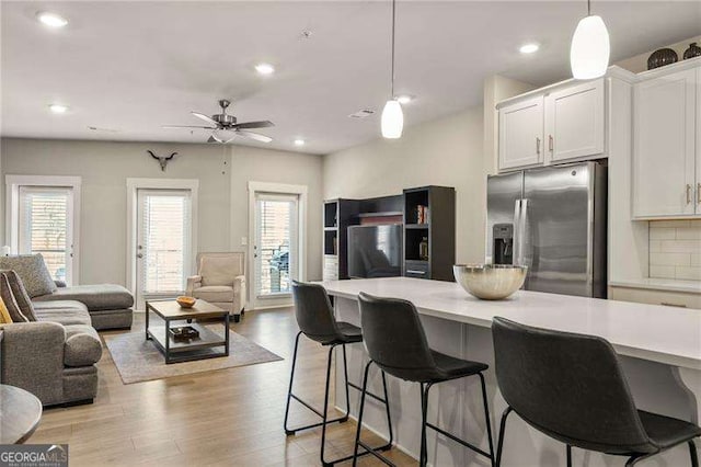 kitchen featuring a breakfast bar area, light countertops, white cabinetry, open floor plan, and stainless steel refrigerator with ice dispenser