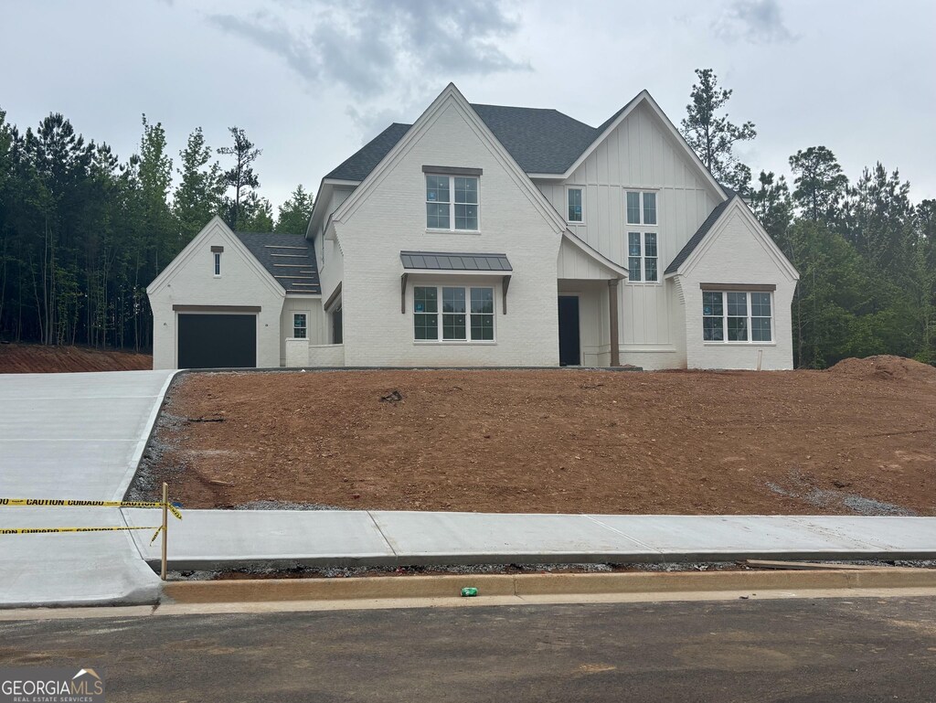 view of front of house with an attached garage, board and batten siding, a standing seam roof, driveway, and metal roof