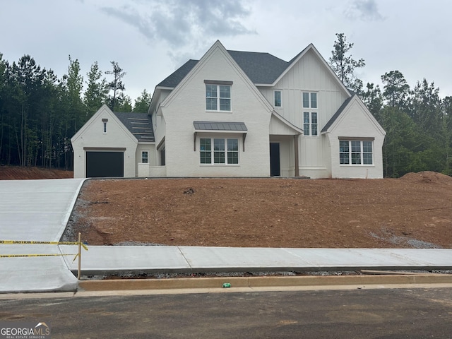 view of front of house with an attached garage, board and batten siding, a standing seam roof, driveway, and metal roof