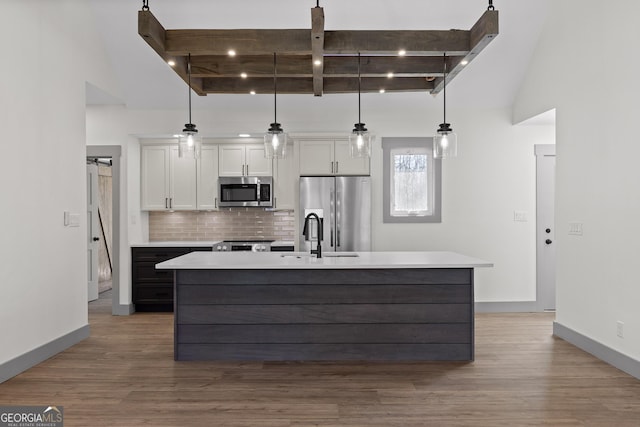 kitchen featuring tasteful backsplash, a center island with sink, wood finished floors, stainless steel appliances, and white cabinetry