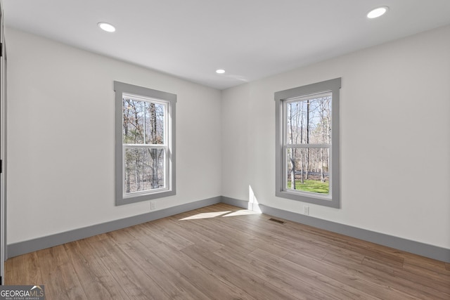 unfurnished room with plenty of natural light, recessed lighting, wood finished floors, and visible vents