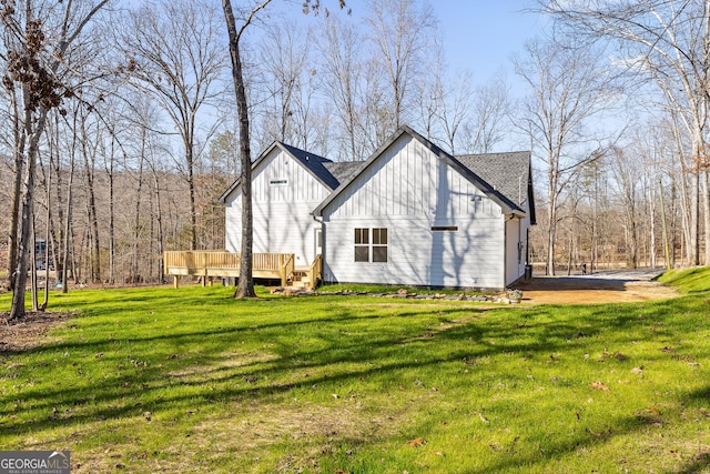 view of side of home featuring a lawn, a shingled roof, board and batten siding, and a deck