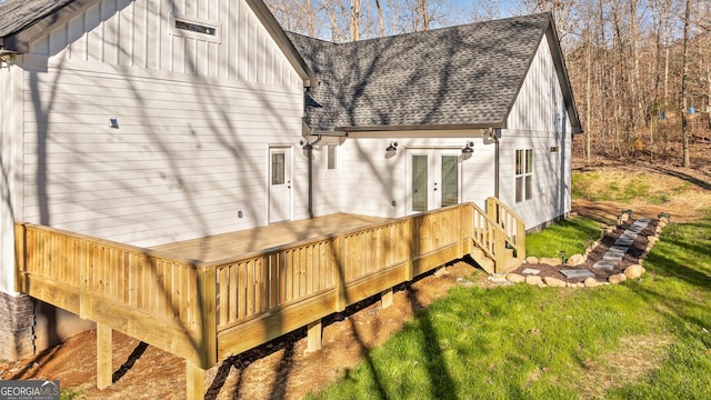 back of property with a shingled roof, board and batten siding, a deck, french doors, and a lawn