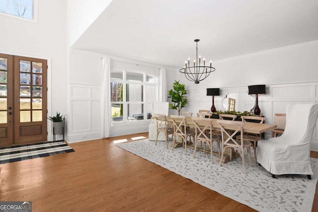 dining space featuring crown molding, wood finished floors, a decorative wall, a chandelier, and french doors