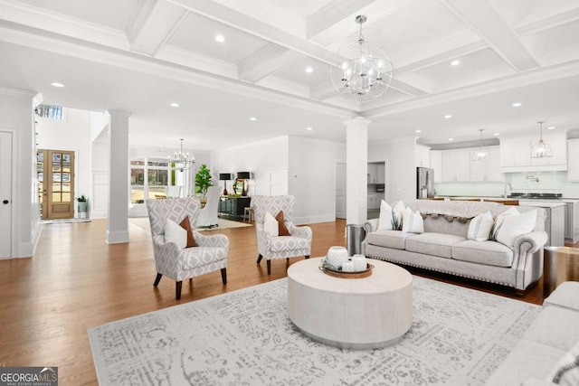 living area featuring light wood-type flooring, coffered ceiling, ornate columns, and a notable chandelier