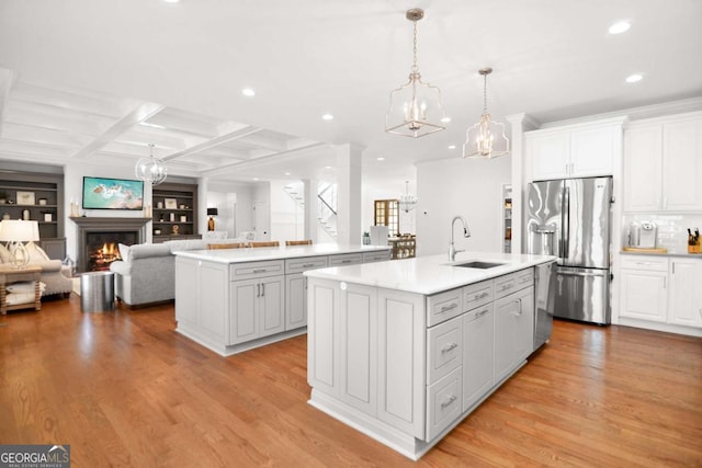 kitchen with a kitchen island with sink, open floor plan, a sink, appliances with stainless steel finishes, and a notable chandelier