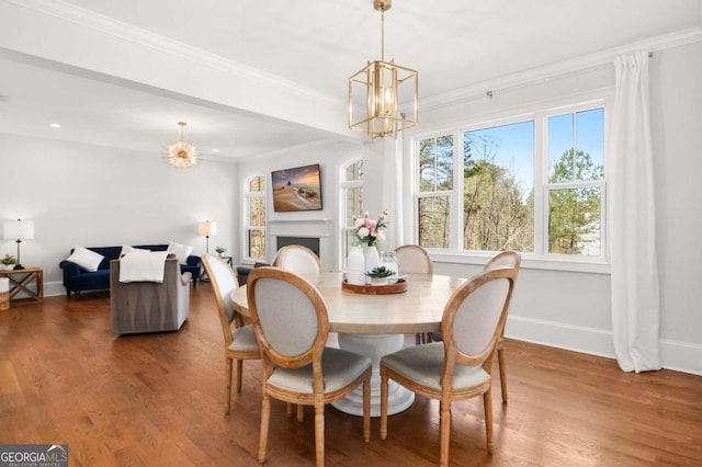 dining space with an inviting chandelier, crown molding, wood finished floors, a fireplace, and baseboards