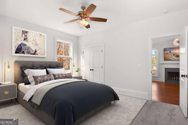 carpeted bedroom featuring ceiling fan, a fireplace with flush hearth, baseboards, and a closet