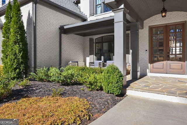 entrance to property featuring french doors, a porch, and brick siding