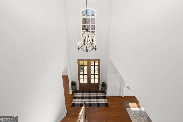 doorway with french doors, a high ceiling, wood finished floors, and a notable chandelier