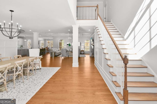foyer featuring light wood-style floors, decorative columns, stairs, and an inviting chandelier